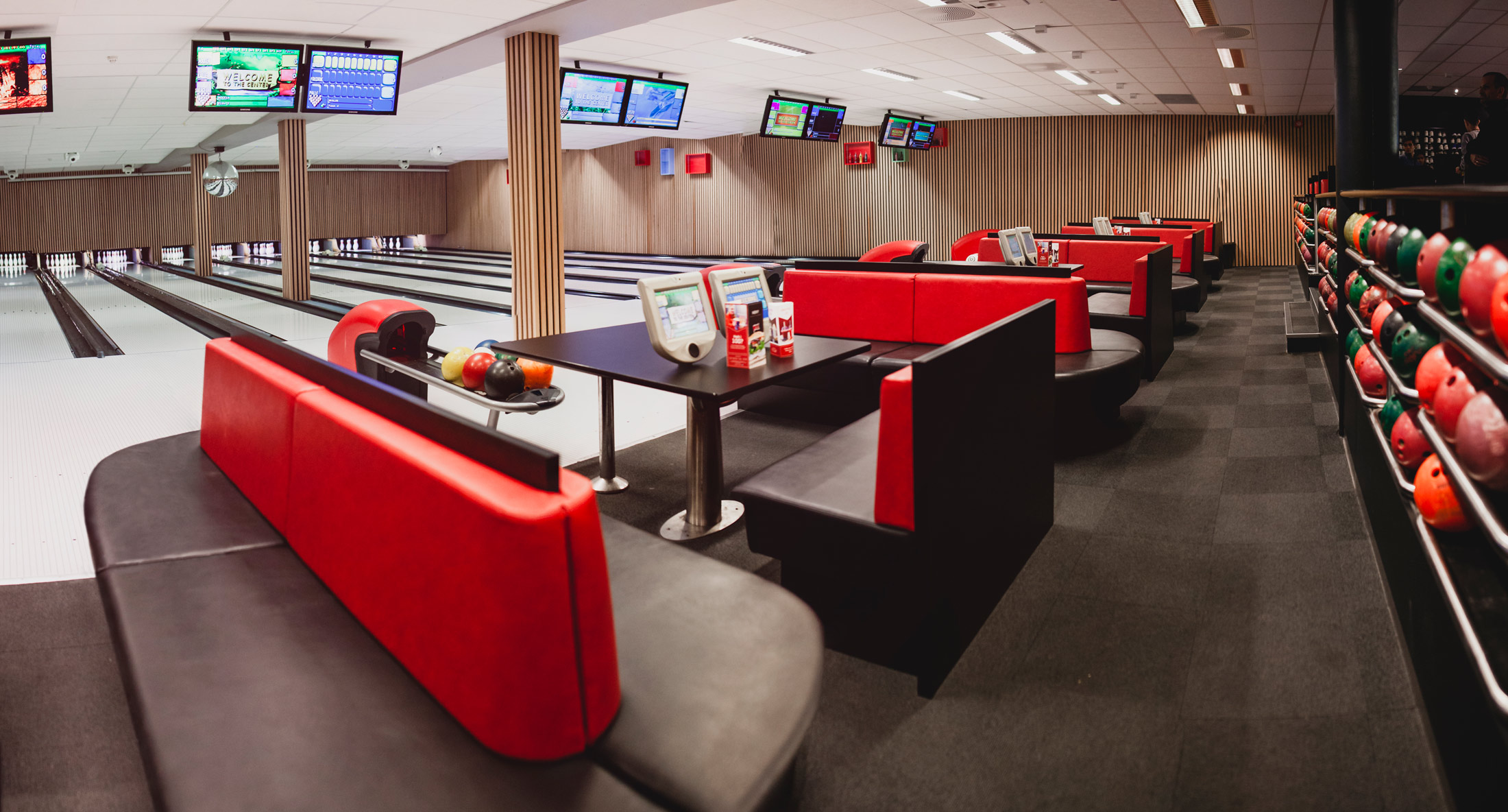 Stadion Bowlings hovedsal — bowling-baner med hvitt gulv, kuleholder med fargerike bowlingkuler i forgrunnen, røde lærsofaer og treverket vegg-paneling rundt sittegruppene